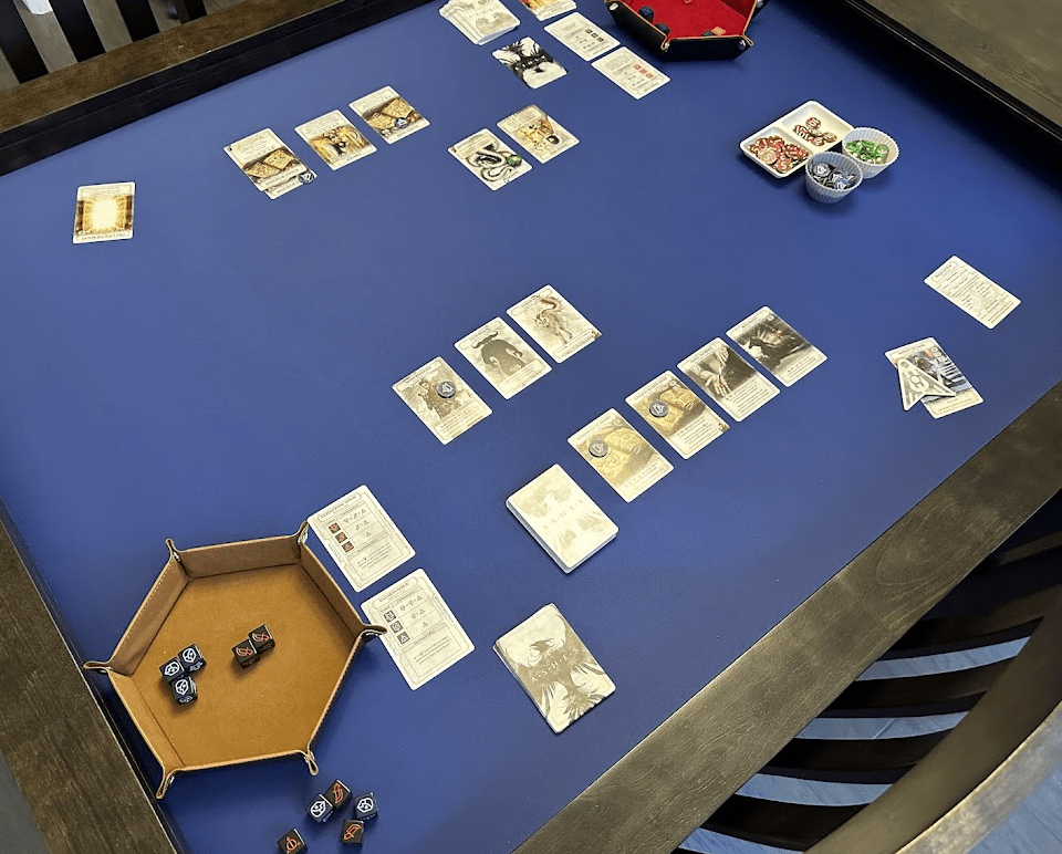 Overhead view of Ashes Reborn game on a blue playmat. Includes cards, dice in dice trays, and chits.