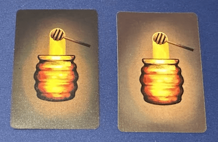 Two card backs showing art of a honeypot and honey dipper. the background colors are slightly different from one another.